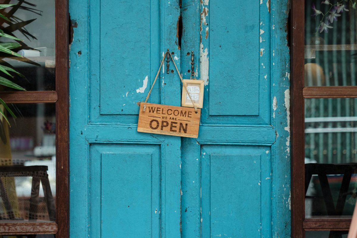 A rustic blue door with a wooden welcome sign indicating the store is open.
